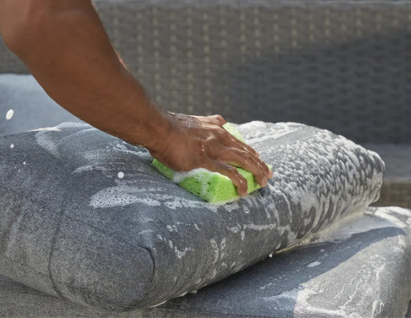 A man washes patio cushions
