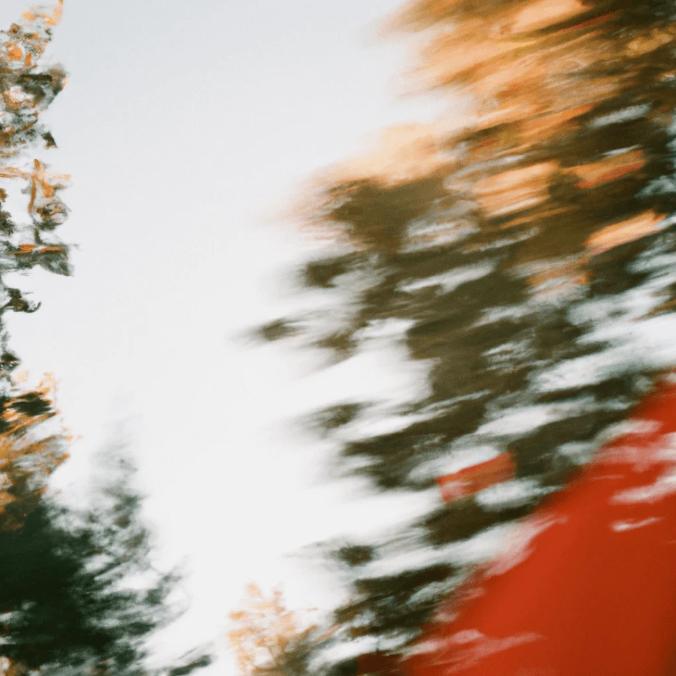 A blurred, abstract photo of trees against a light sky. The motion effect creates streaks of green and brown foliage, with a hint of red in the lower corner, giving the image a sense of movement and energy.