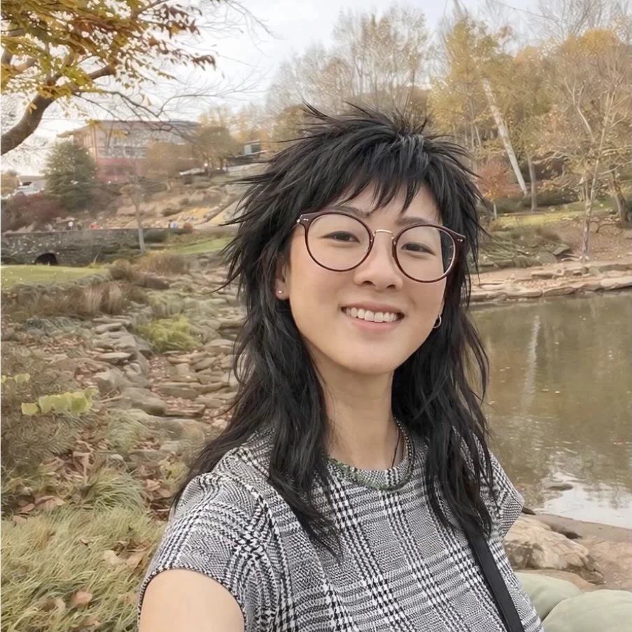 A person taking a selfie outdoors by a lake.