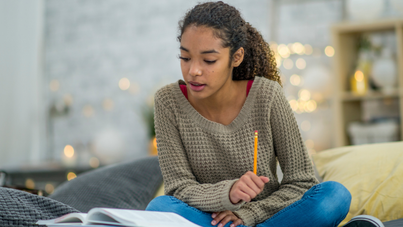 female-student-reading-textbook-on-bed