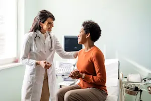 A doctor talks to a patient that is sitting on a medical bed.