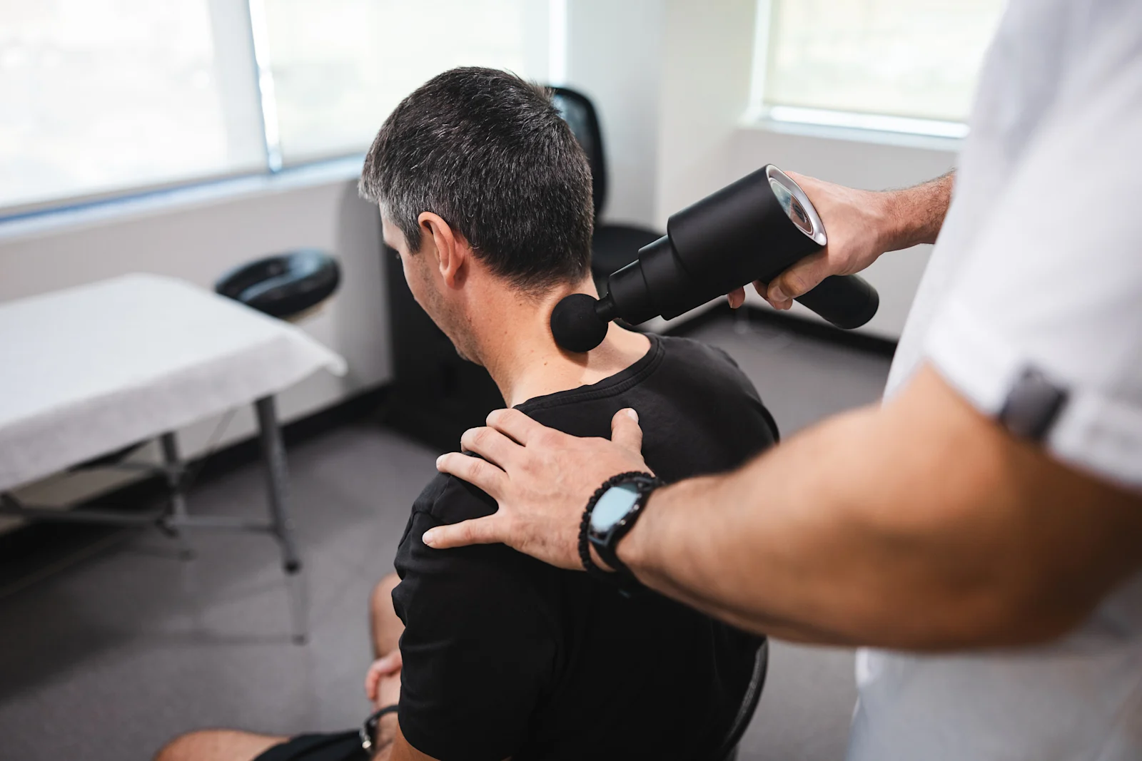 Man receiving neck treatment with massage gun