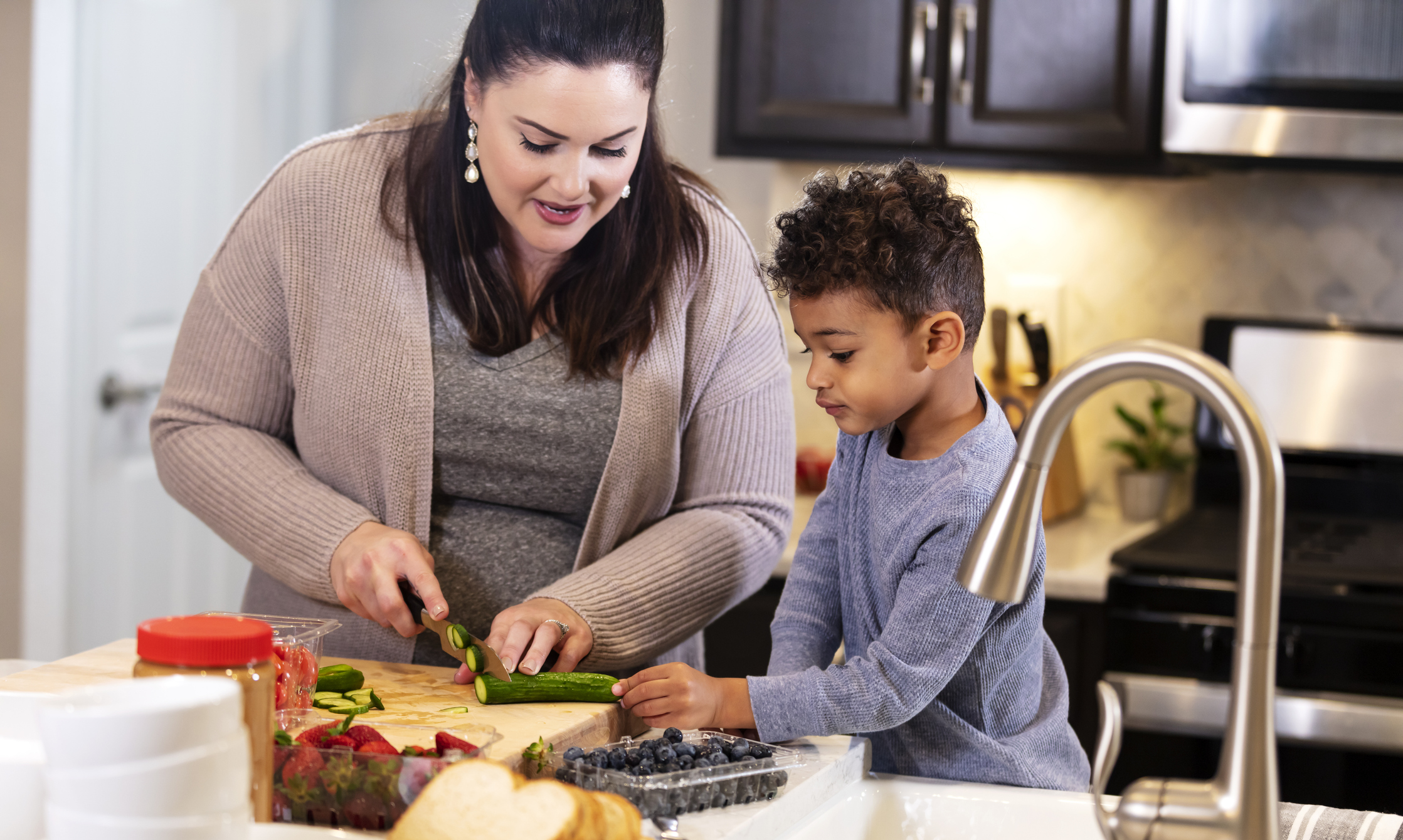 Adult helping child cut cucumber