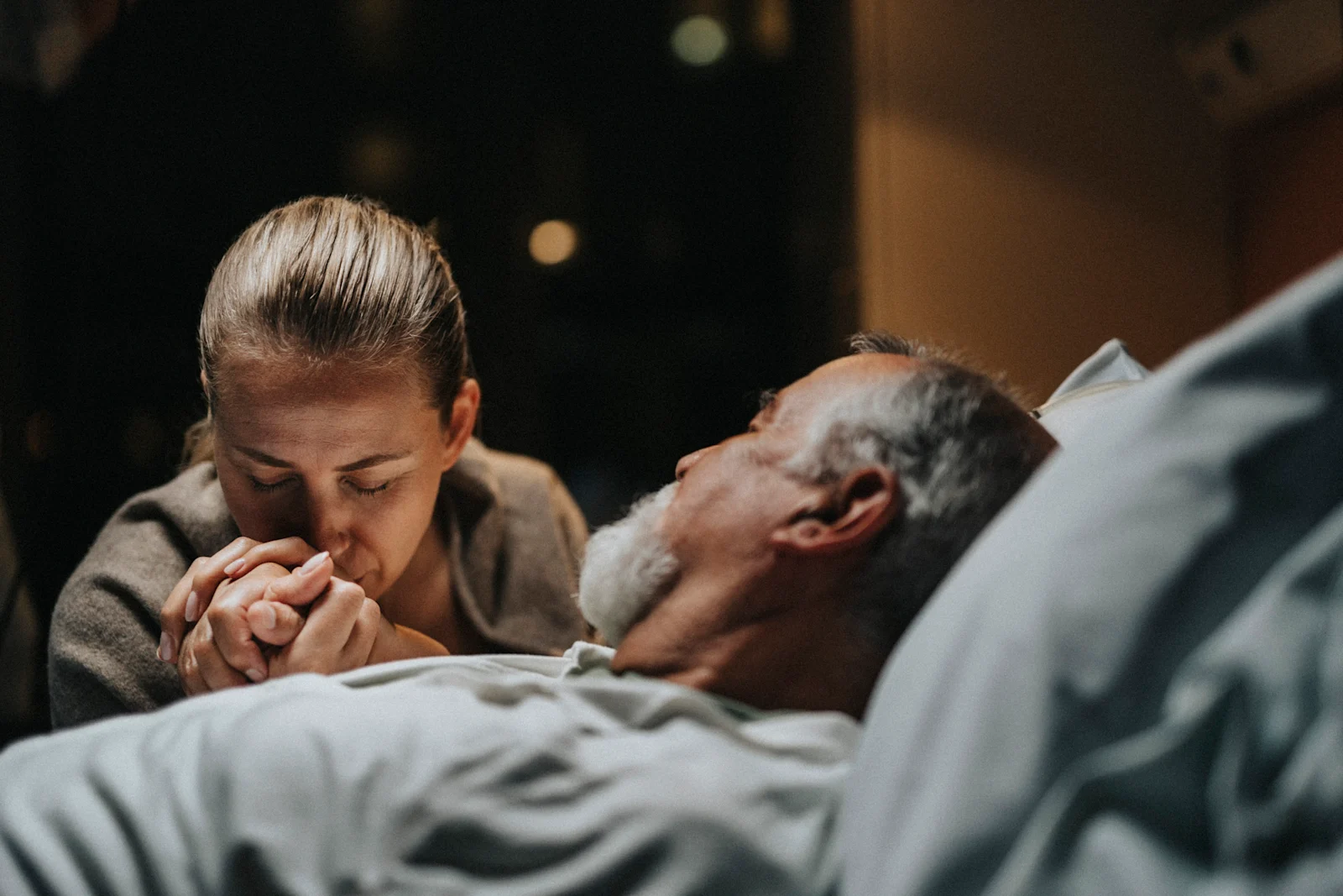 Woman kissing elderly man's hand as he lies in bed