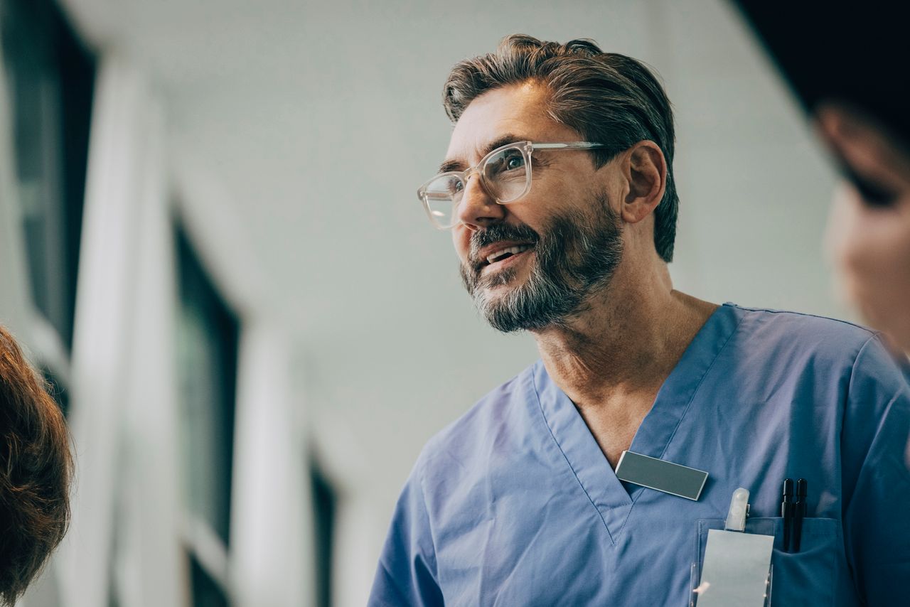 Man with glasses & scrubs smiling