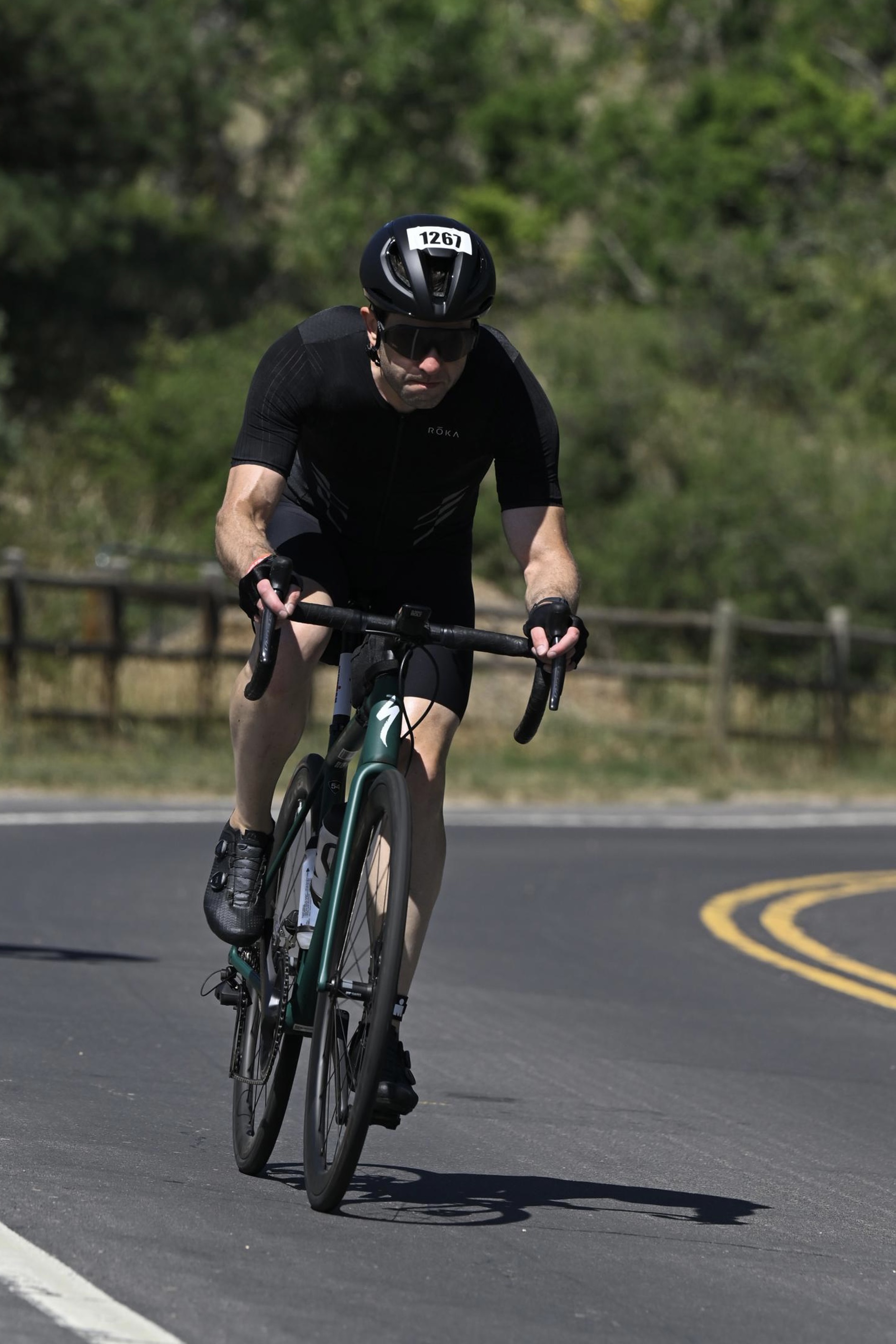 Me, riding a green Specialized Aethos bike on a country road. I'm wearing a black Roka tri suit, black gloves, dark sunglasses, and a black helmet with the number 1267 on it.