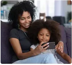 Assises sur un canapé, une femme et sa fille regardent du contenu sur un téléphone.