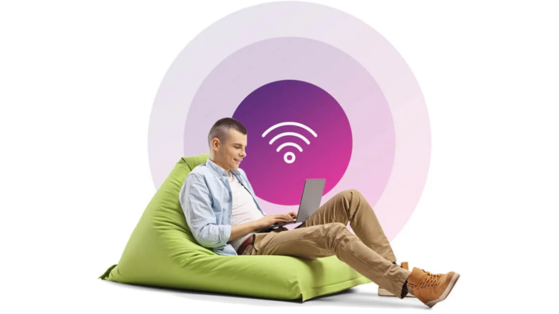  Un jeune homme assis sur un fauteuil poire utilise un ordinateur portable et une icône Wi-Fi représentant un signal fort se trouve au-dessus de lui..