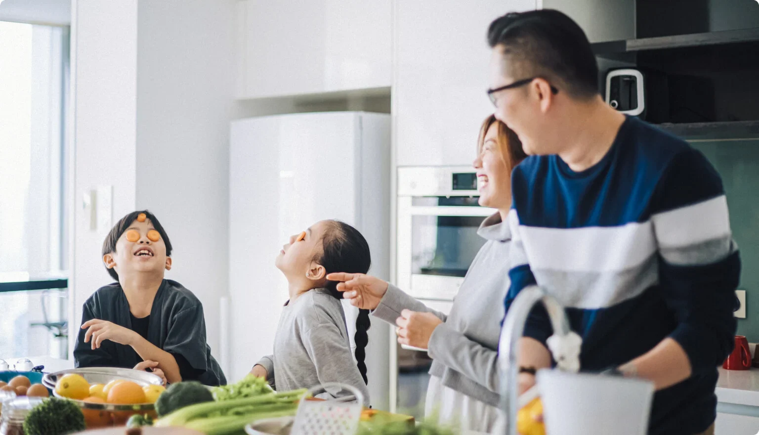 A family is seen cooking together and laughing int he kitchen.
