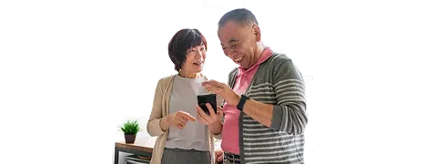 Two seniors stand side-by-side, smiling and looking at a mobile phone screen.