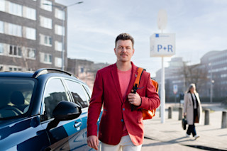 Man met telefoon naast een Hely-deelauto.