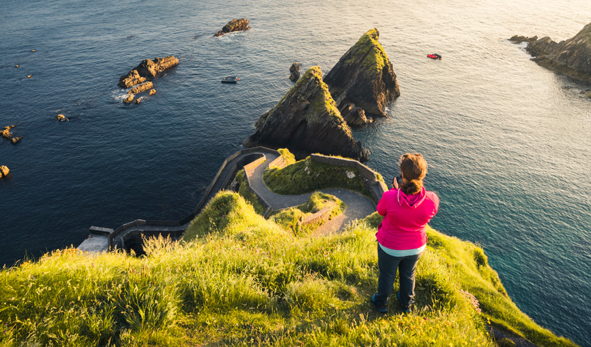 Female hiker in a pink hoodie taking in the scenic cliffside view of Ireland’s Dunquin Pier.