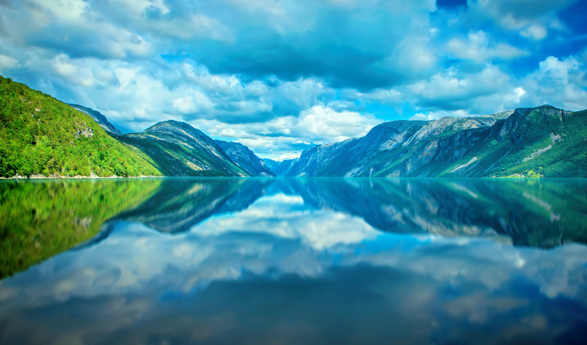 A serene fjord surrounded by lush green mountains and dramatic clouds.