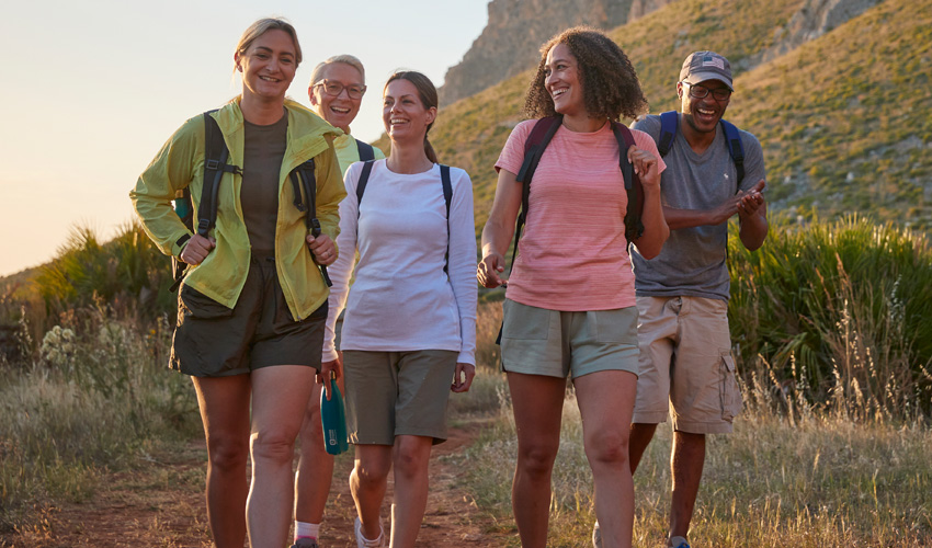 A diverse group of five people hiking a scenic country trail at on a summer day. 