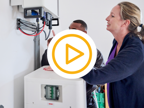 Saman monteur geeft uitleg aan een klant over installatie van de dyness tower pro thuisbatterij en een video play button