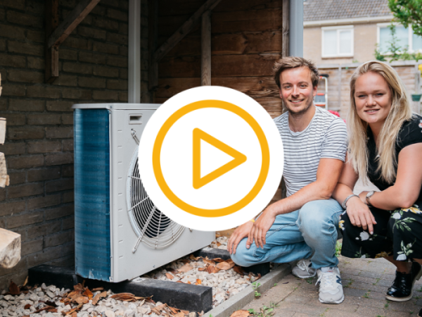 Hurkend stel poseert lachend naast warmtepomp in de tuin met video play button 
