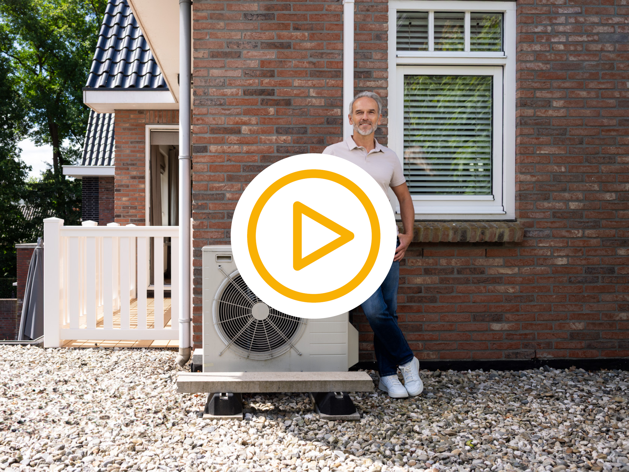 Mn poserend naast een warmtepomp op dak van de eerste verdieping met video play button 