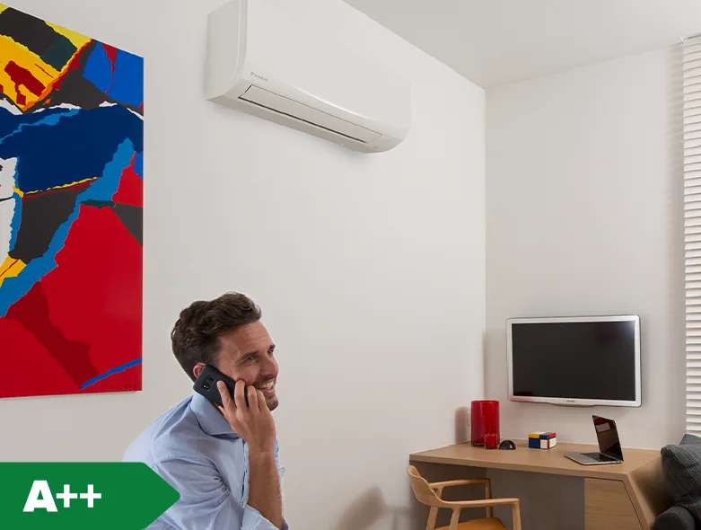 Airco model Sensira Daikin aan de muur met lachende man die aan het bellen is in zijn thuis kantoor