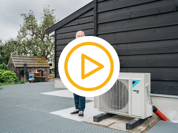 Klant staat blij naast zijn nieuwe warmtepomp buiten en een video play button