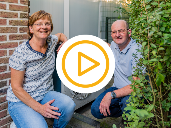 2 blije klanten zitten gehurkt naast hun nieuwe warmtepomp en een video play button