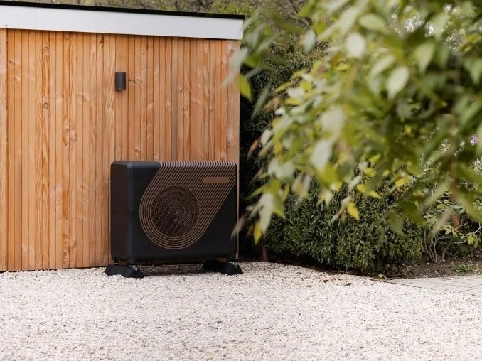 De Weheat sparrow hybride/all-electric warmtepomp in koper kleur in de tuin naast een schuurtje in de zon