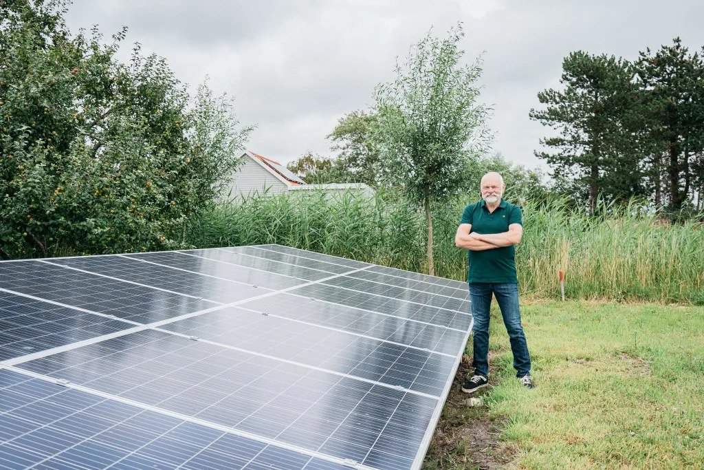 Klant staat trots naast zonnepanelen in de tuin