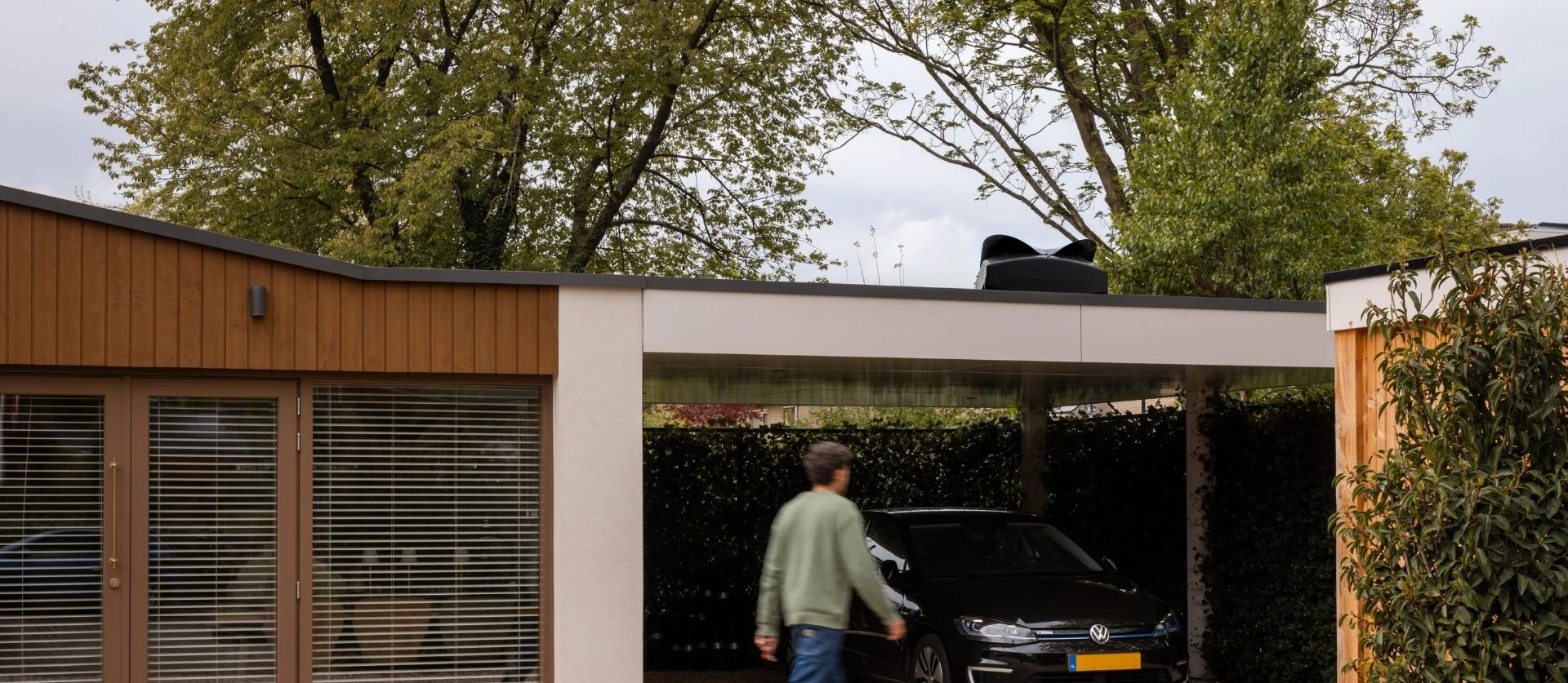 Blackbird Weheat warmtepomp op het dak van een carport in een tuin boven een volkswagen met een man die langsloopt door de tuin
