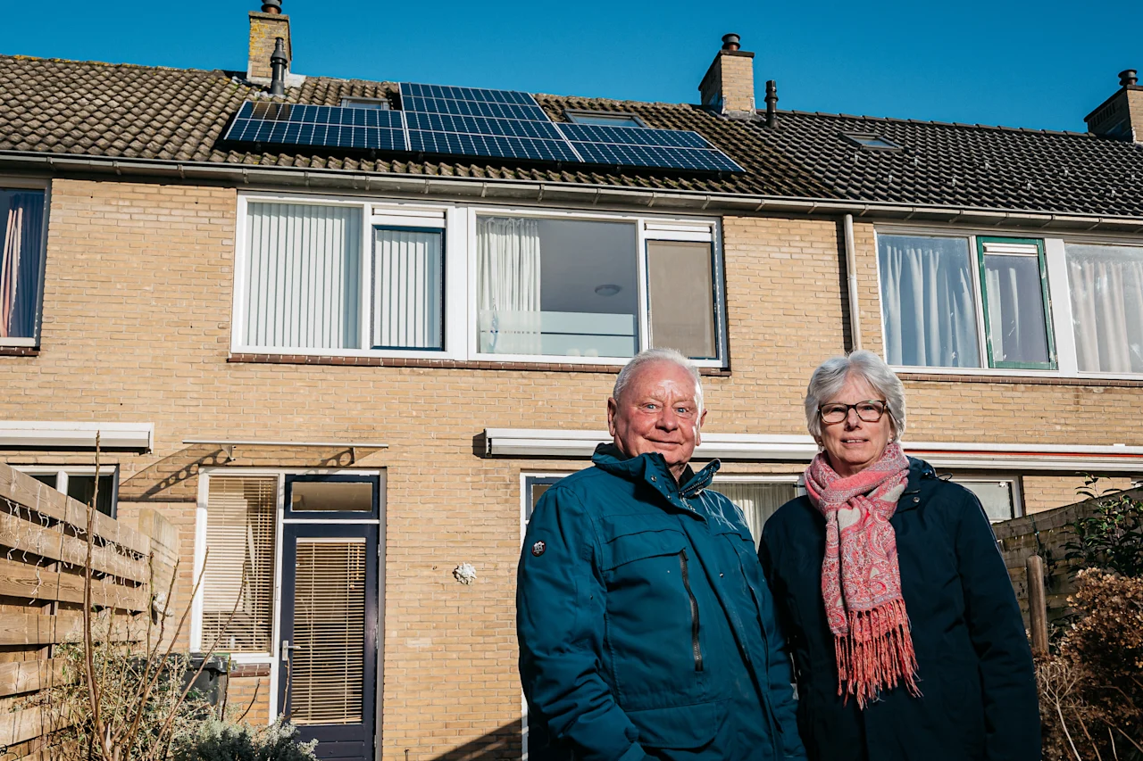Poserend stel staat tevreden voor hun huis waarvan zonnepanelen van de saman groep op het dak liggen.
