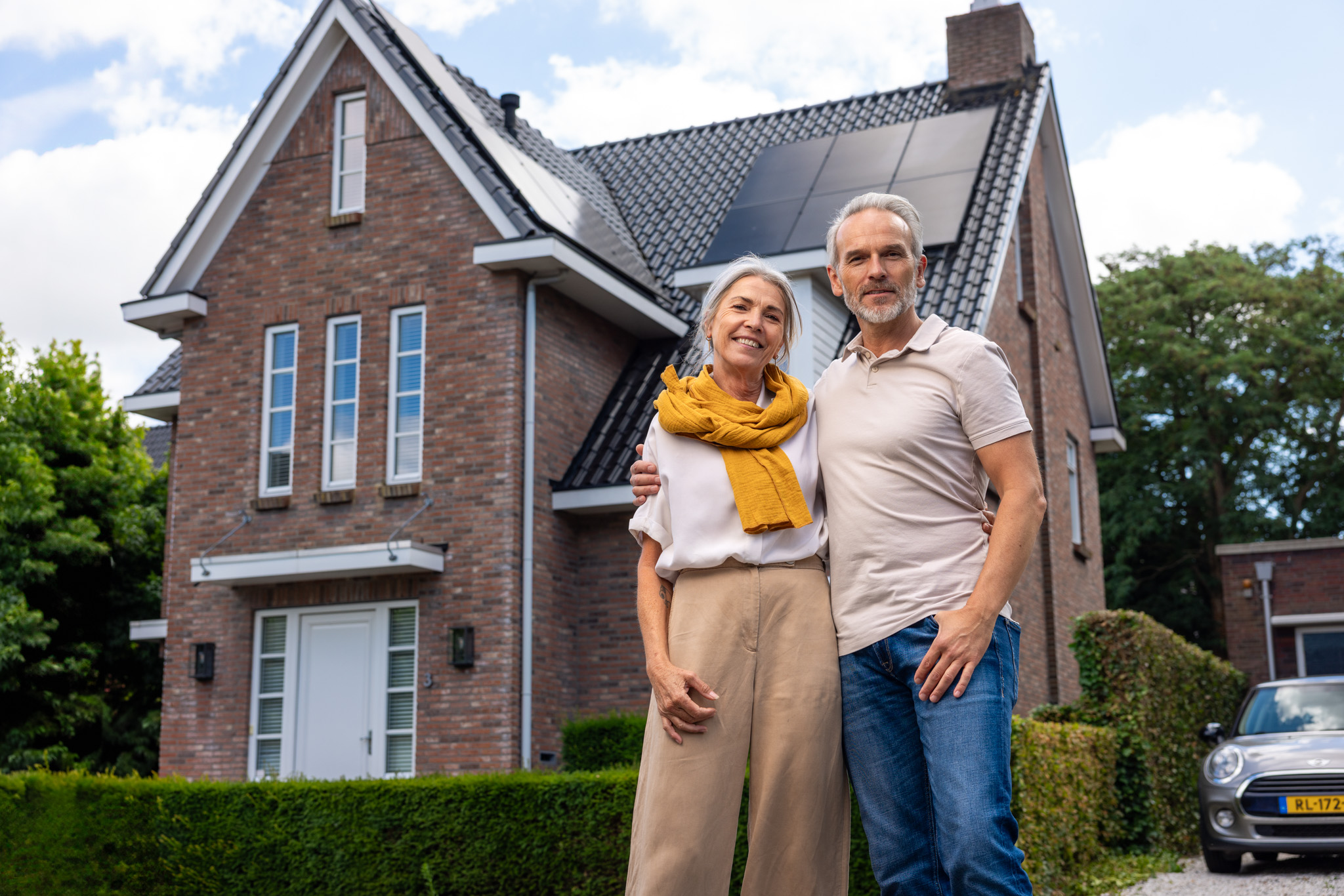 Foto stel glimlachend en omhelzend voor hun huis met nieuwe zonnepanelen