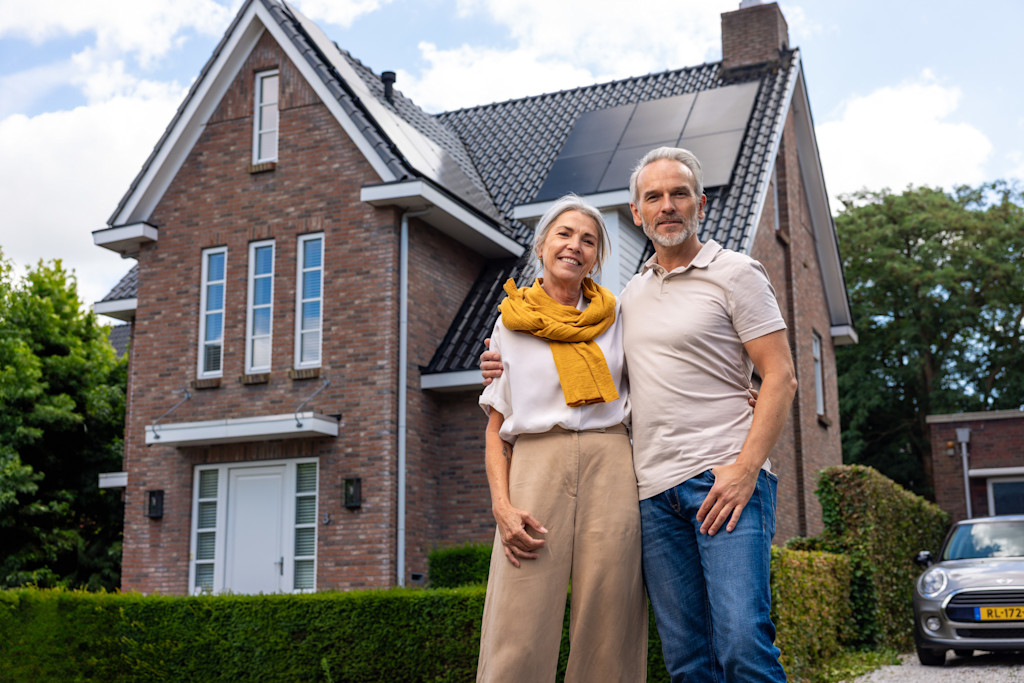 Foto stel glimlachend en omhelzend voor hun huis met nieuwe zonnepanelen