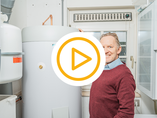 Klant staat blij naast zijn warmtepomp binnen unit boiler en een video play button