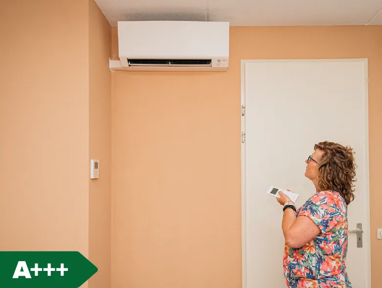 Airco model Perfera Daikin aan de muur met een vrouw met afstandsbediening in haar hand gericht op de airco