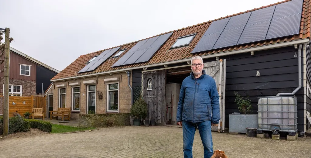 Meneer staat met zijn hond voor zijn huis waarvan het dak gevuld is met zonnepanelen