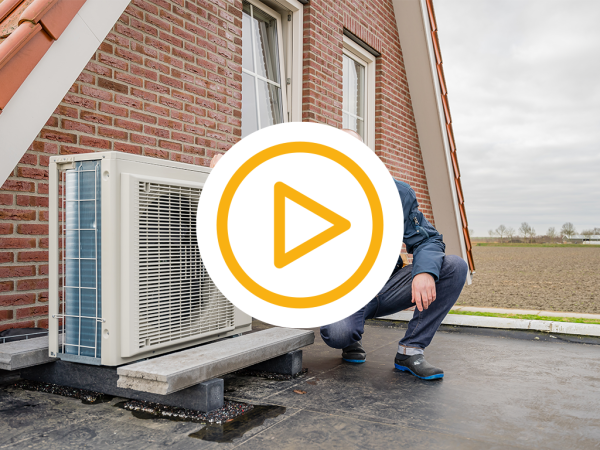 Blije klant zit gehurkt op een dak naast zijn warmtepomp en een video play button