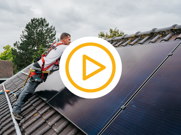 Saman monteur installeert zonnepanelen op een schuin dak en een video play button