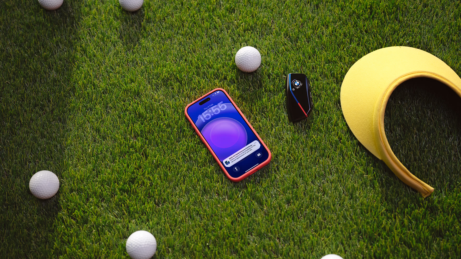 Smartphone next to a BMW key, golf balls and a visor, all laying on the grass