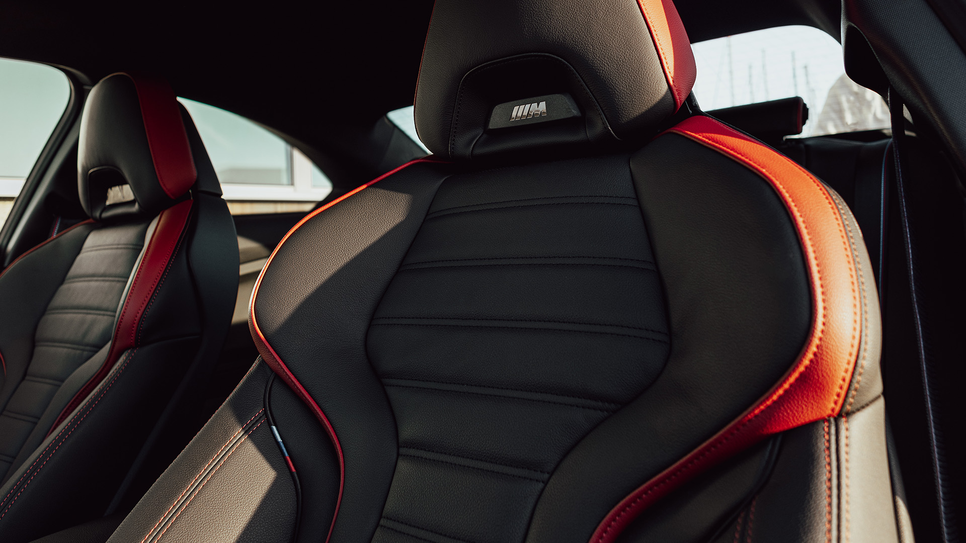 Close-up of a black and red BMW sports car seat with detailed stitching, ergonomic design, and visible logo on the headrest.