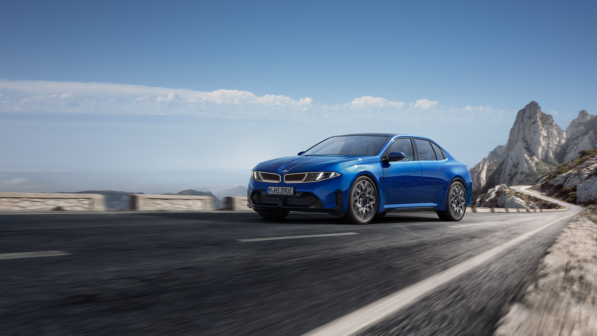 Blue BMW i3 saloon driving on a mountain road, with motion blur and rocky clifs in the background.