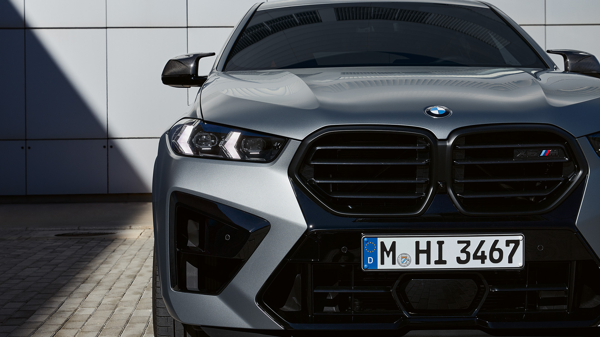 Front view of a silver BMW car parked on a paved surface in front of a modern building.