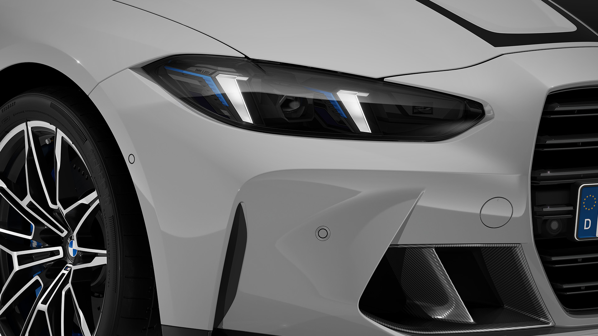 Close-up of the front left side of a white BMW car, showing the headlight, part of the grille, and a portion of the front wheel with intricate rim design.