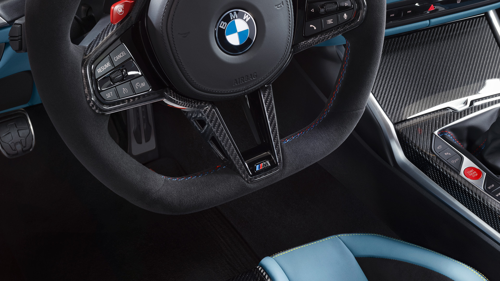 Interior view of a BMW car showing the steering wheel, digital dashboard with navigation, speedometer and part of the driver's seat in blue and black upholstery.