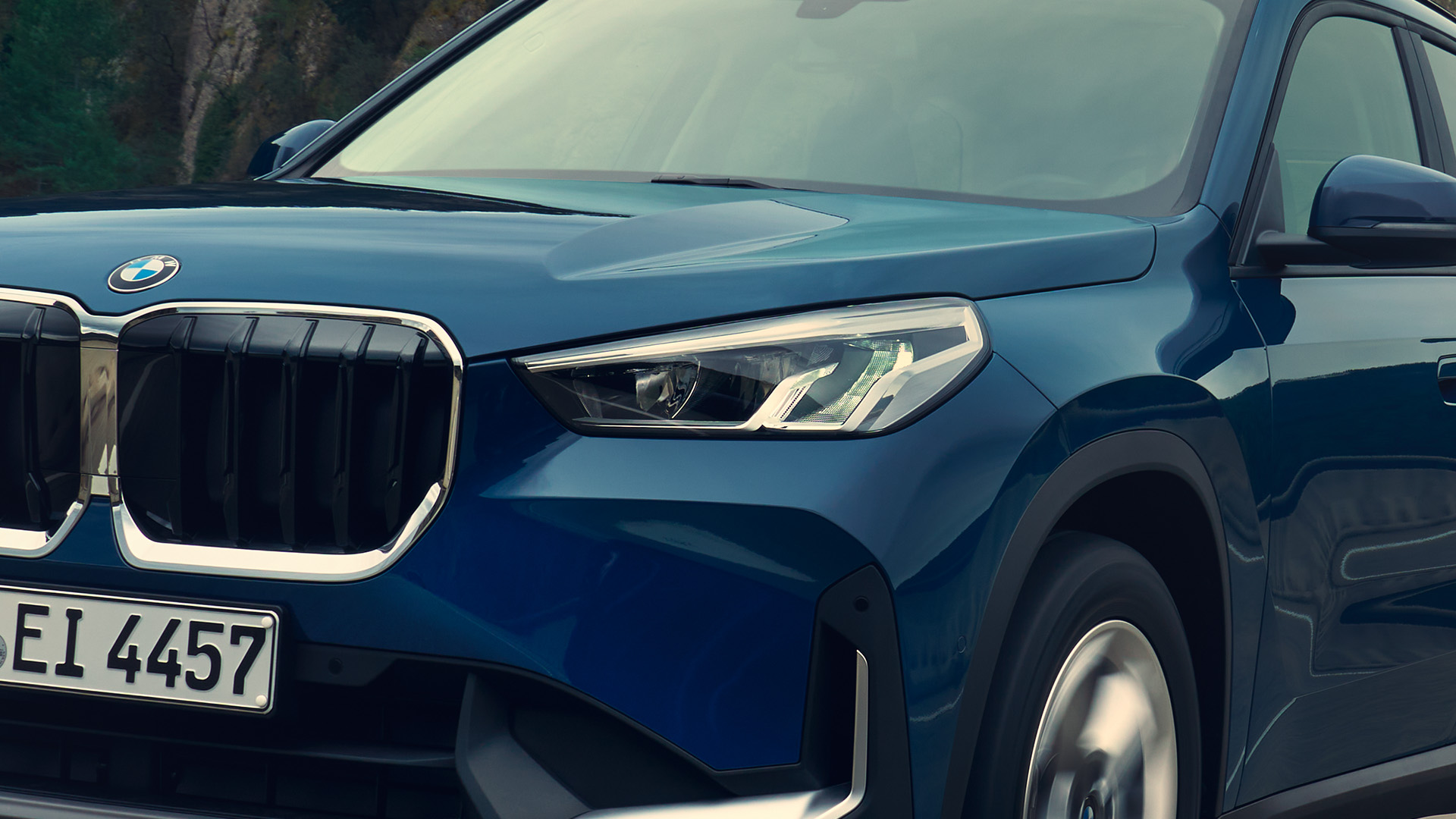 Front view of a blue BMW SUV showing the grille, headlights, and part of the front wheel