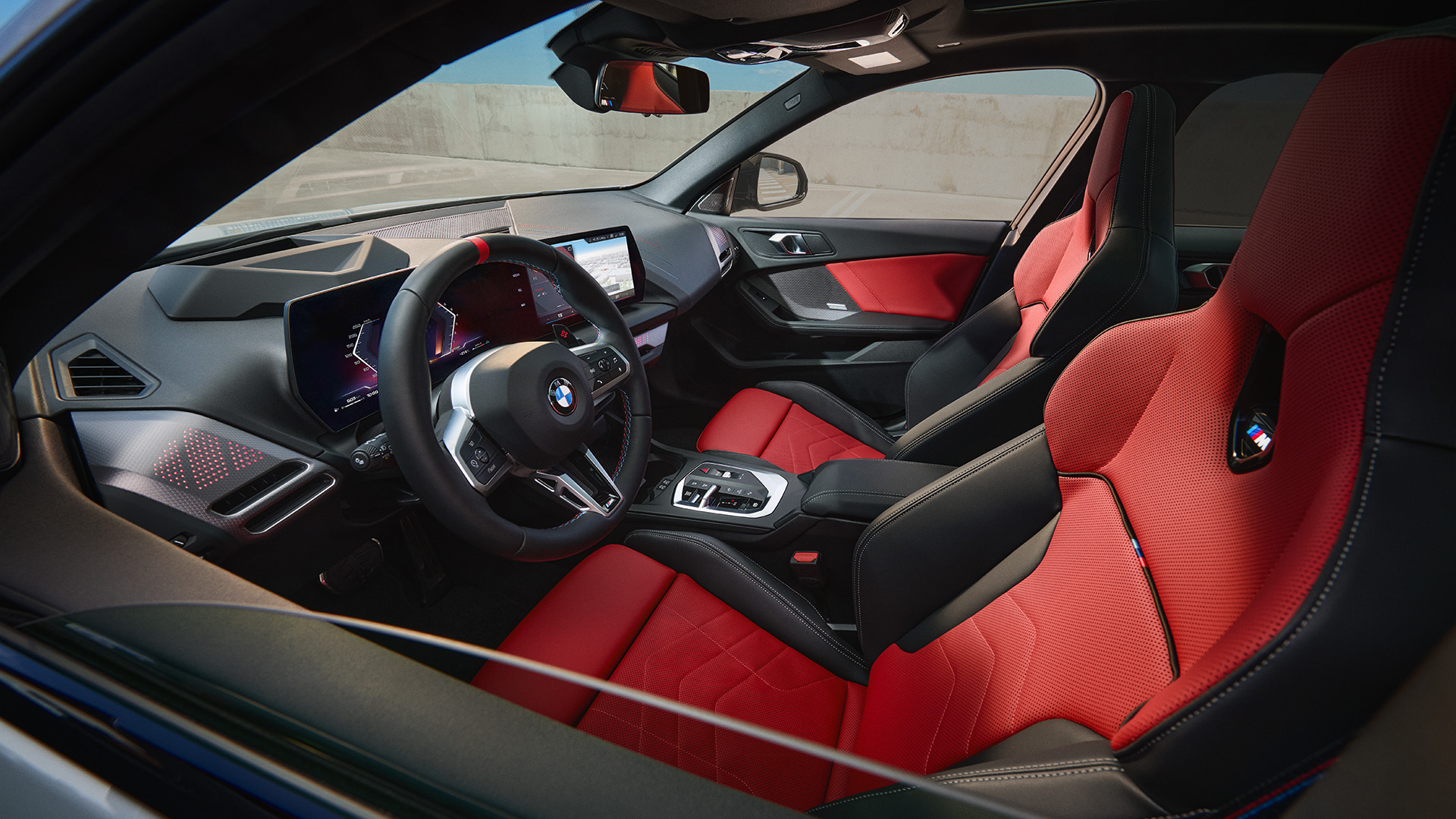 Interior of a modern BMW car with red and black leather seats, a sleek dashboard with digital displays, and a steering wheel featuring the BMW logo.