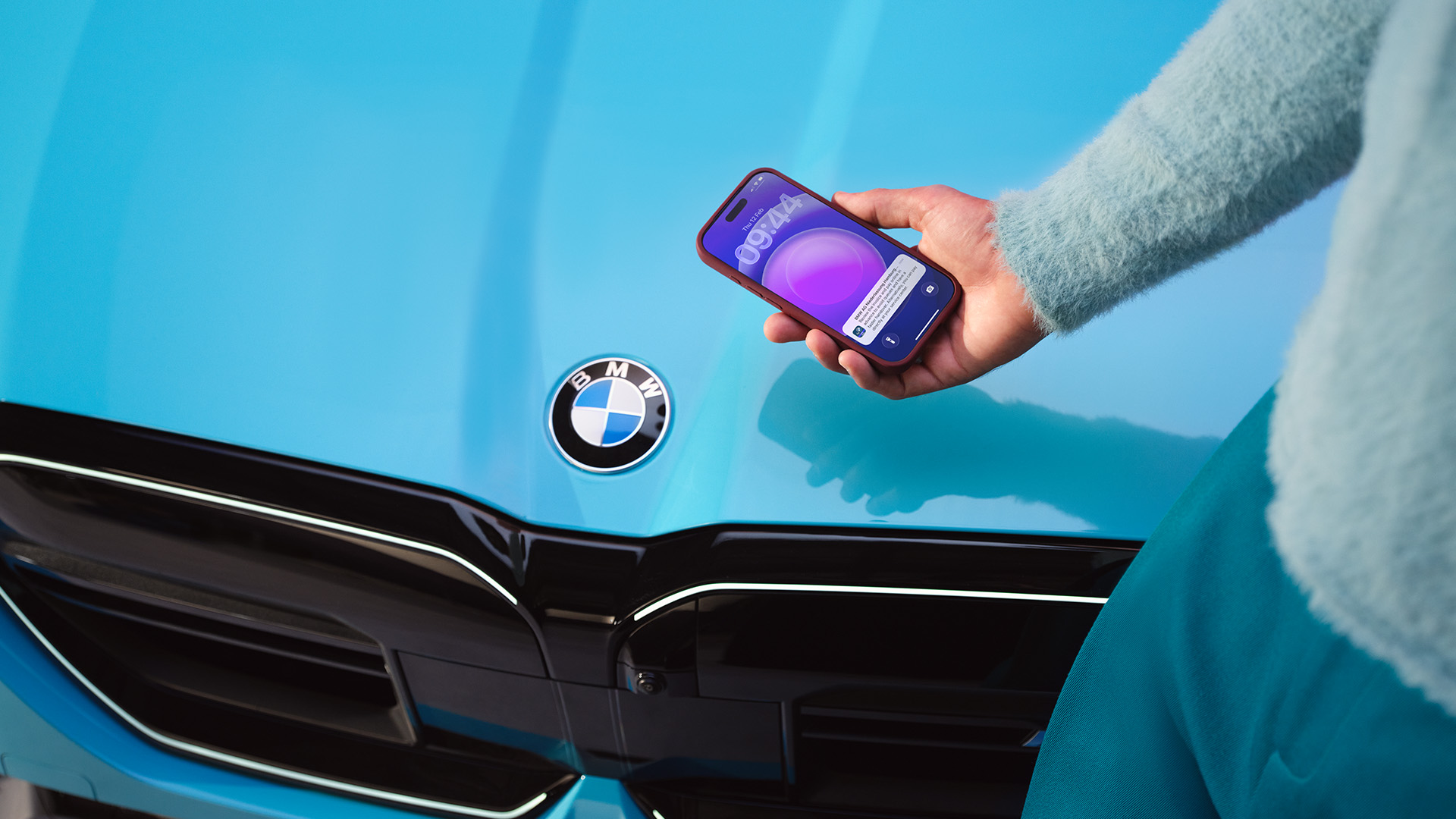 Person holding purple smartphone outside blue BMW.