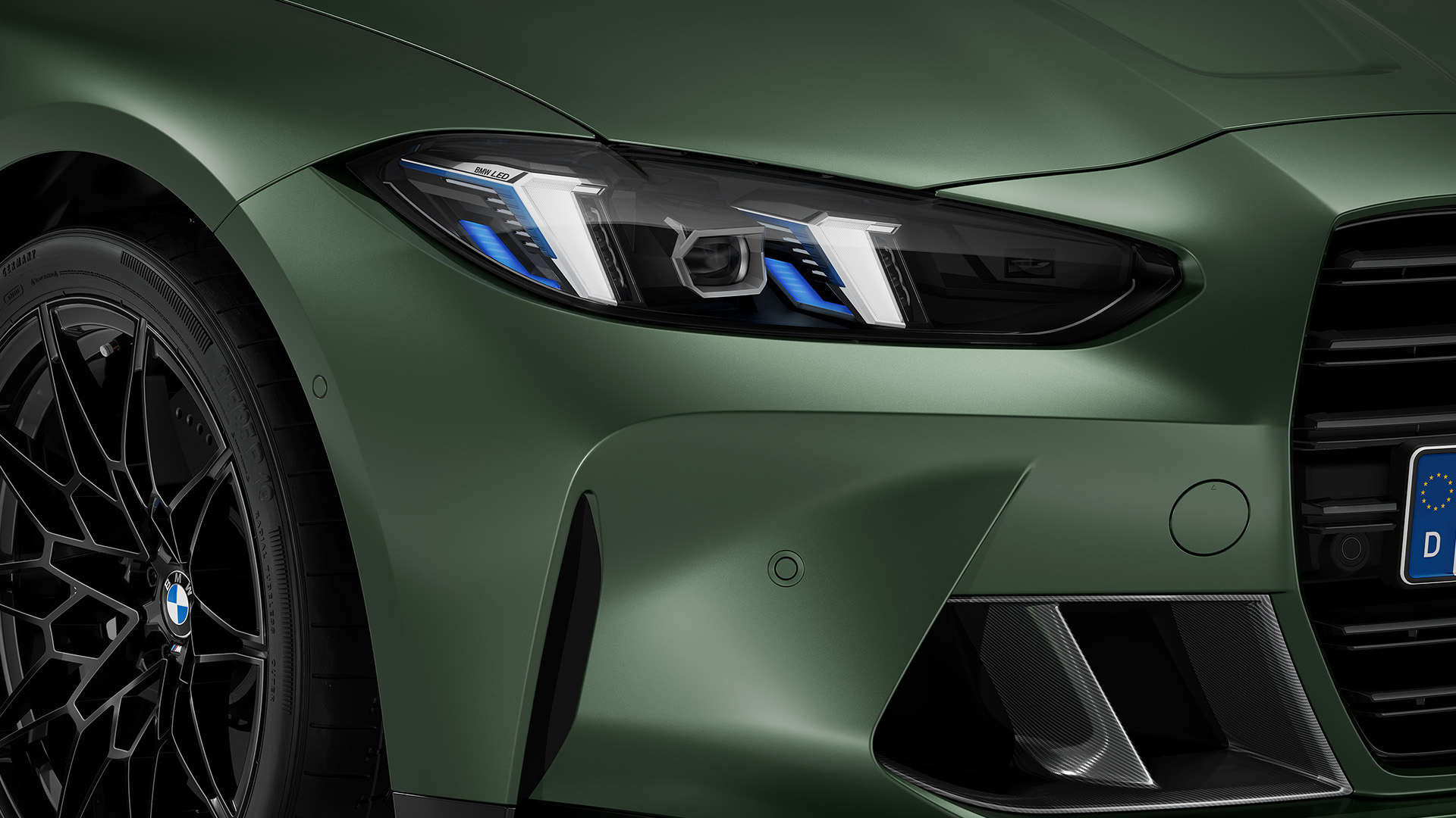 Close-up of the front left side of a green BMW car, showcasing the headlight, black alloy wheel, and part of the grille.