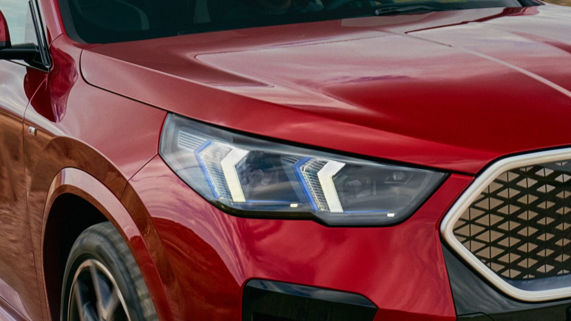 Close-up of the front right side of a red car, focusing on the headlight and part of the grille.