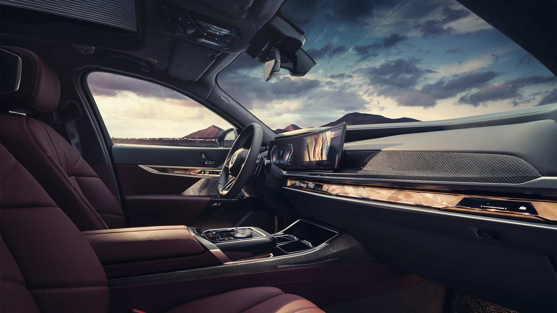 Interior of a luxury BMW car with maroon leather seats, a sleek dashboard, and a panoramic view of mountains through the windshield.