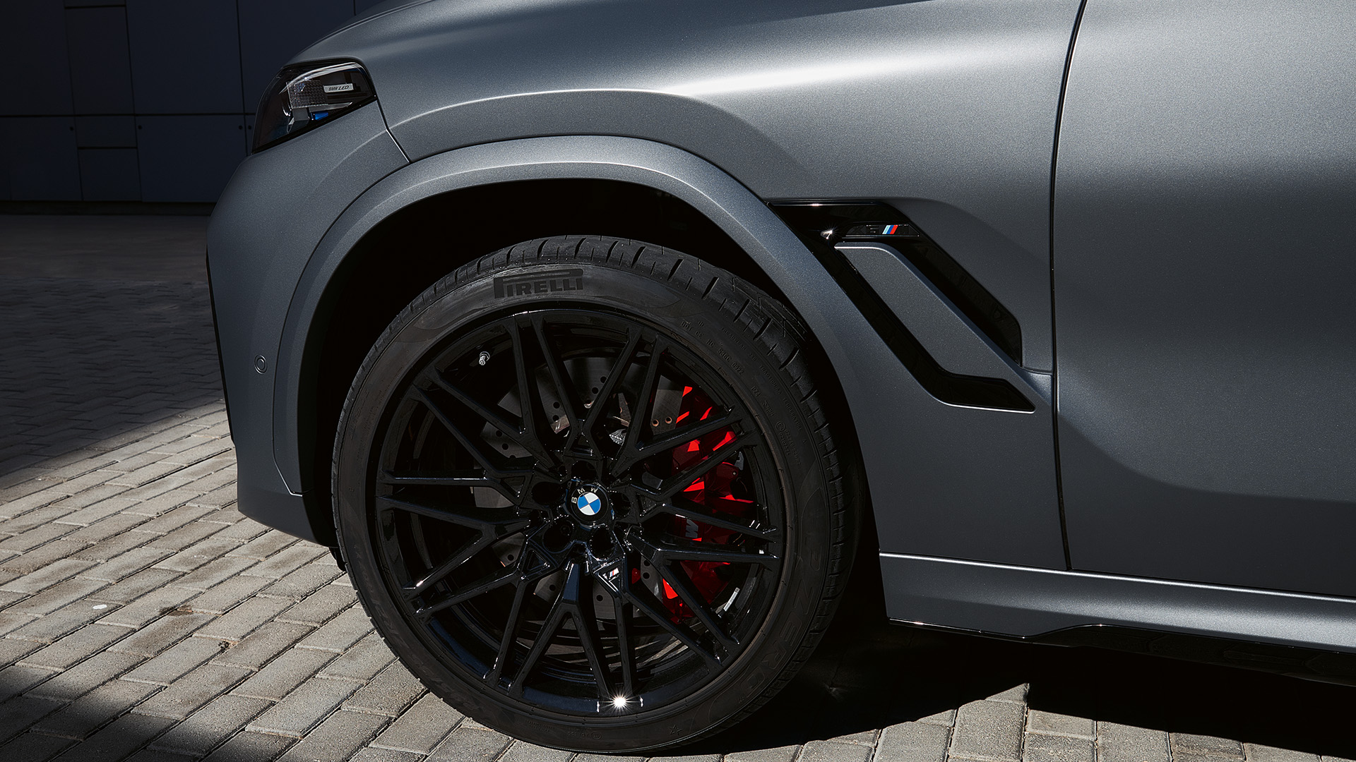 Close-up of the front left side of a gray BMW car, showing the black alloy wheel with red brake calipers.