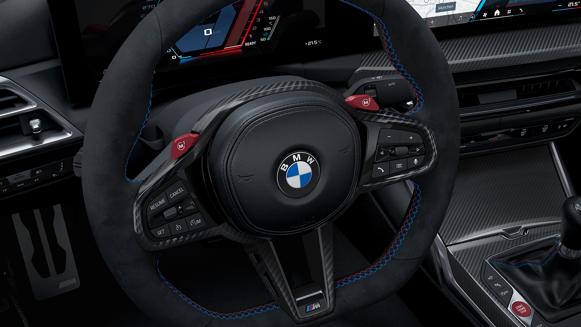 Close-up view of a BMW car's interior, focusing on the steering wheel with the BMW logo, dashboard displays showing navigation maps and vehicle information, and part of the gear shift.