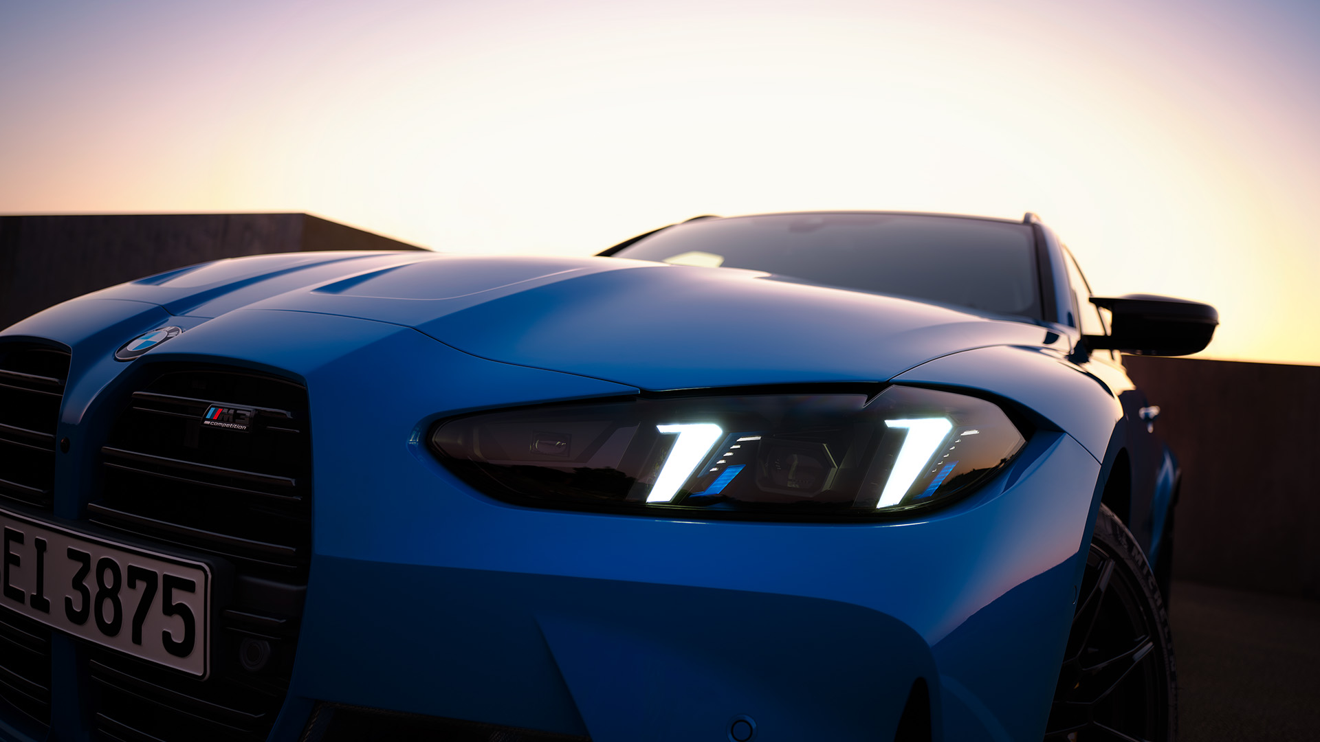 Close-up of a blue BMW car with illuminated headlights at sunset.